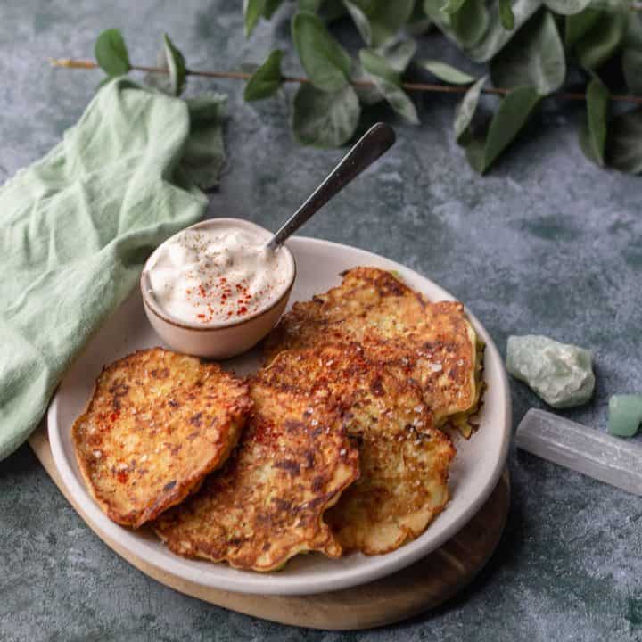 Zucchini & Potato Pancakes on a beige plate with a pot of sour cream